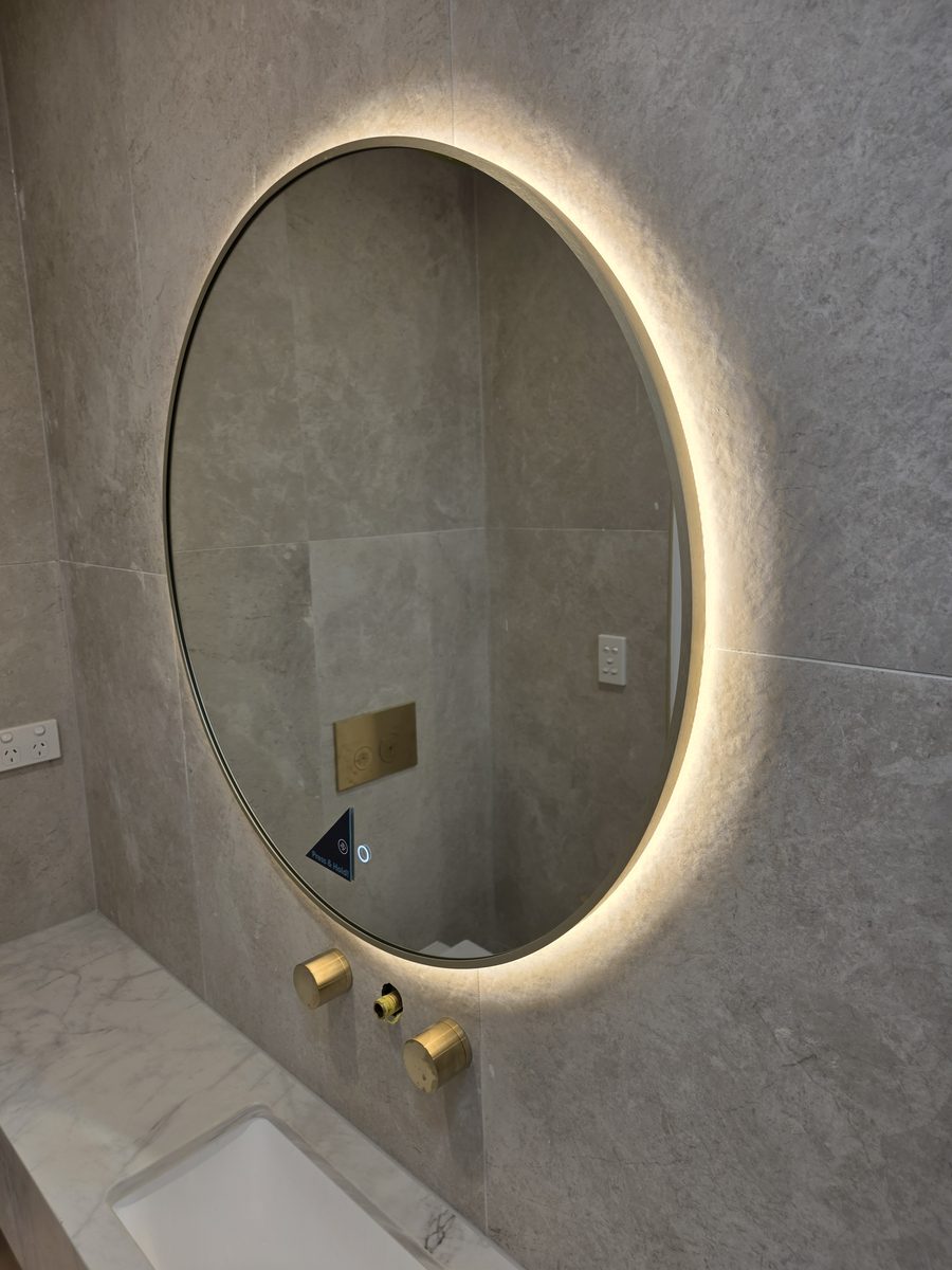 Round back-lit bathroom mirror over a marble vanity at a high-end duplex in Picnic Point