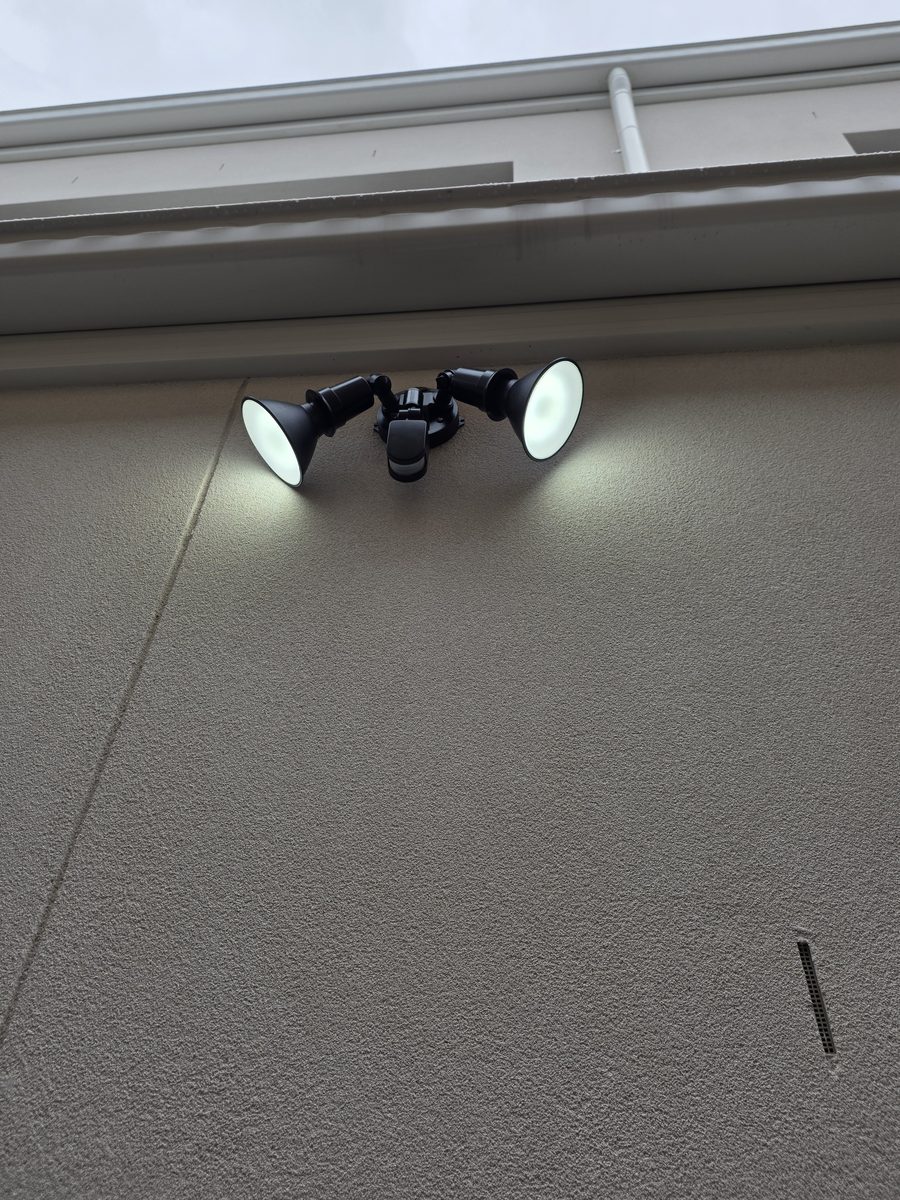 Twin black exterior sensor spotlights lit under the eave, Picnic Point duplex